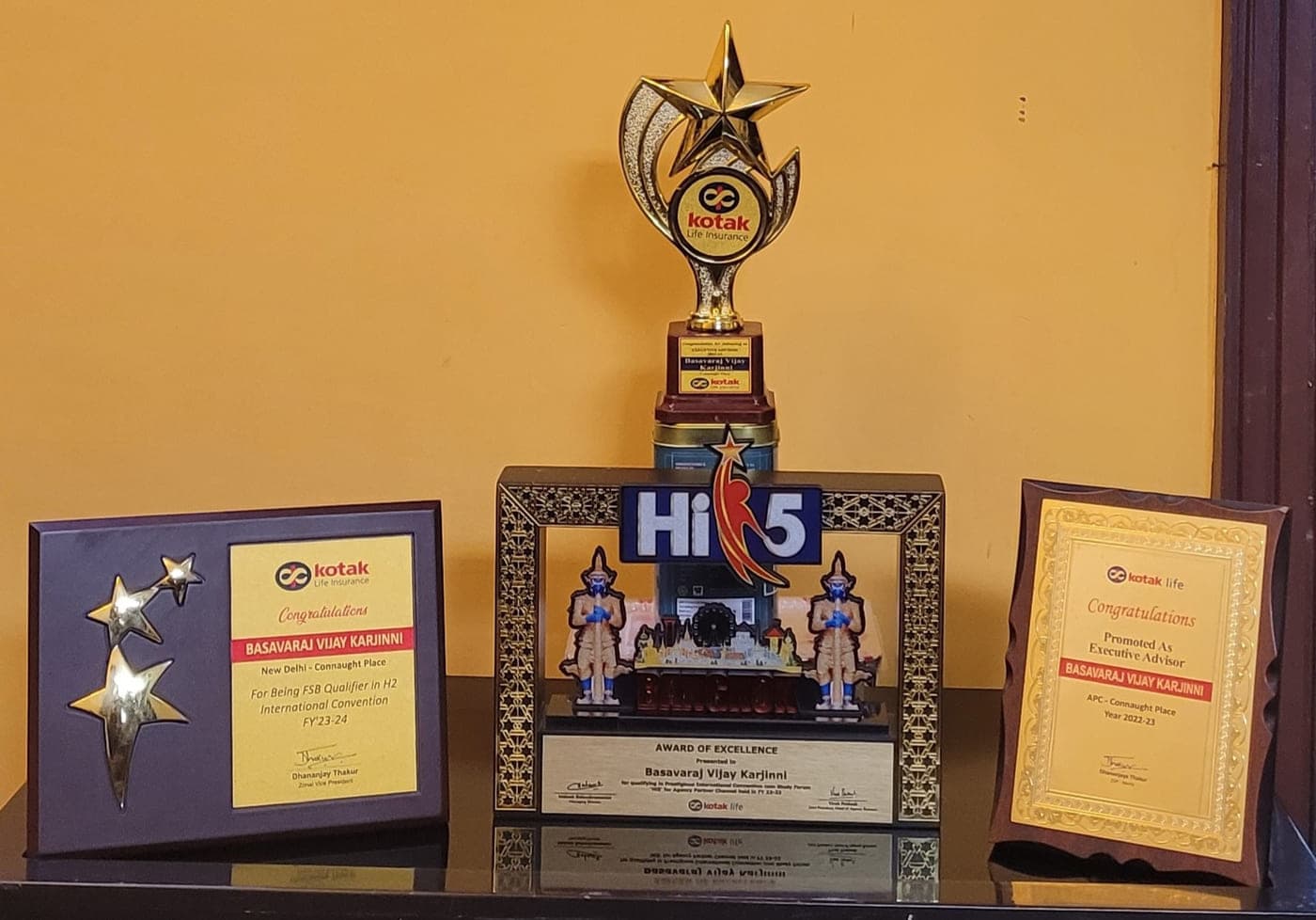 Kotak Life awards on display — the FSB Qualifier star plaque, the Hi 5 Award of Excellence from Bangkok, and the Executive Advisor promotion certificate.
